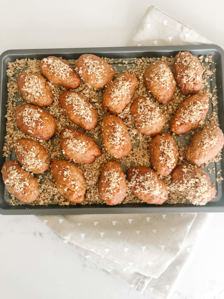 melomakarona on a cookie sheet sprinkled with ground walnuts and honey syrup