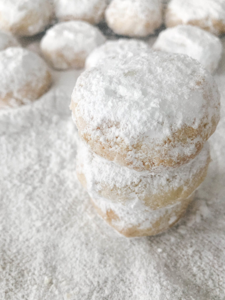 three greek almond cookies stacked on top of each other and sprinkled with icing sugar