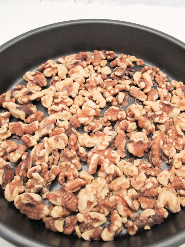 toasted whole walnuts on a black circular baking pan.