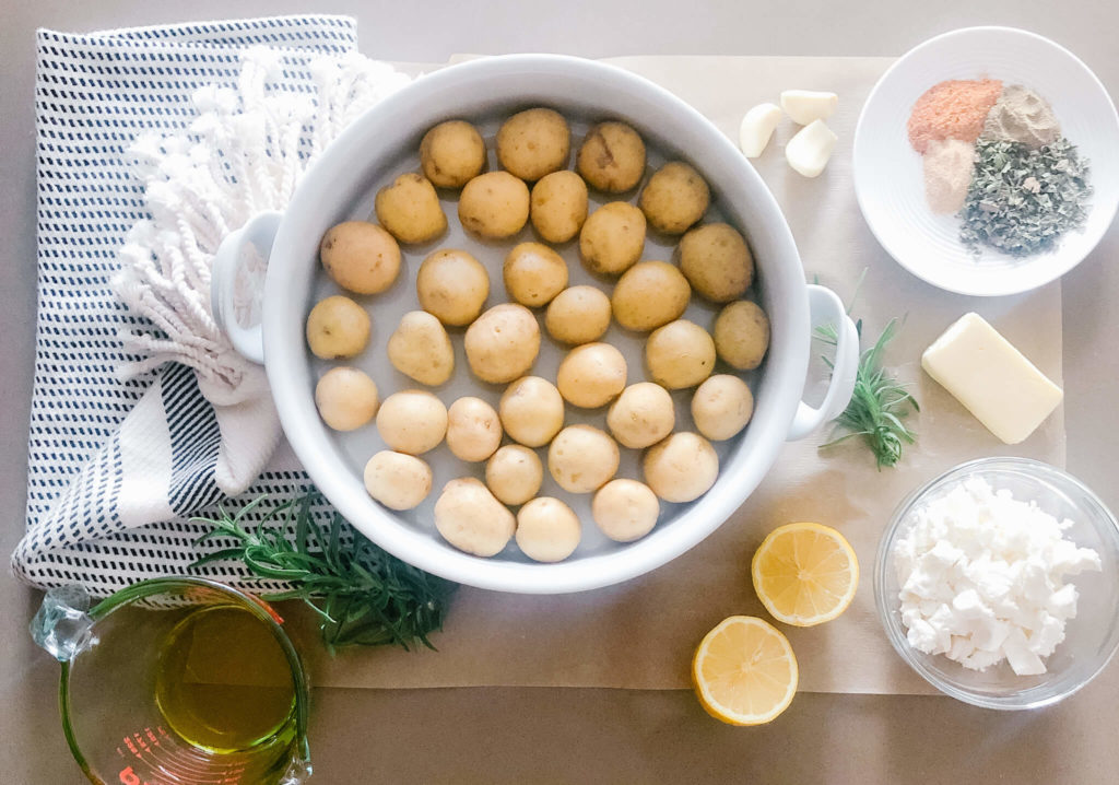 tiny potatoes in a baking dish. A small bowl with olive oil, seasonings, lemon and garlic.