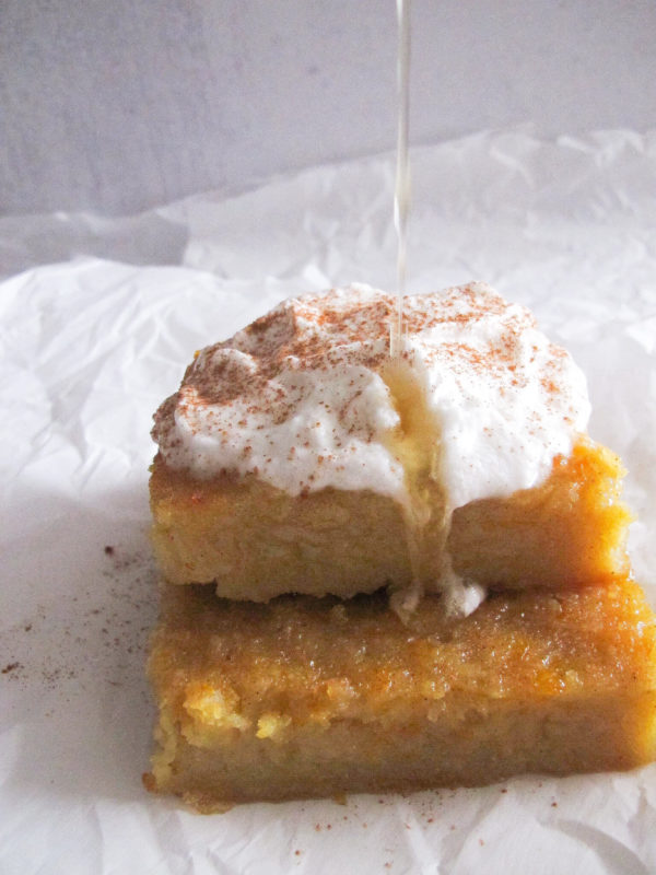 two pieces of portokalopita topped with whipped cream, cinnamon, and orange syrup