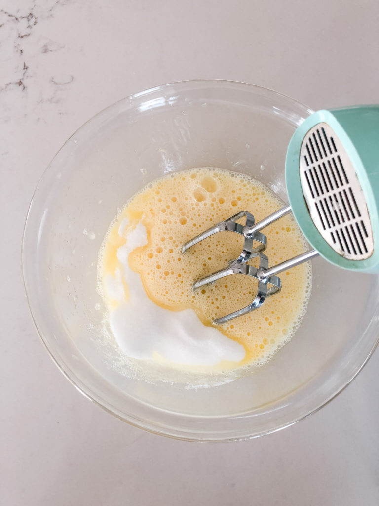 sugar and eggs in a glass bowl getting mixed with an electric mixer