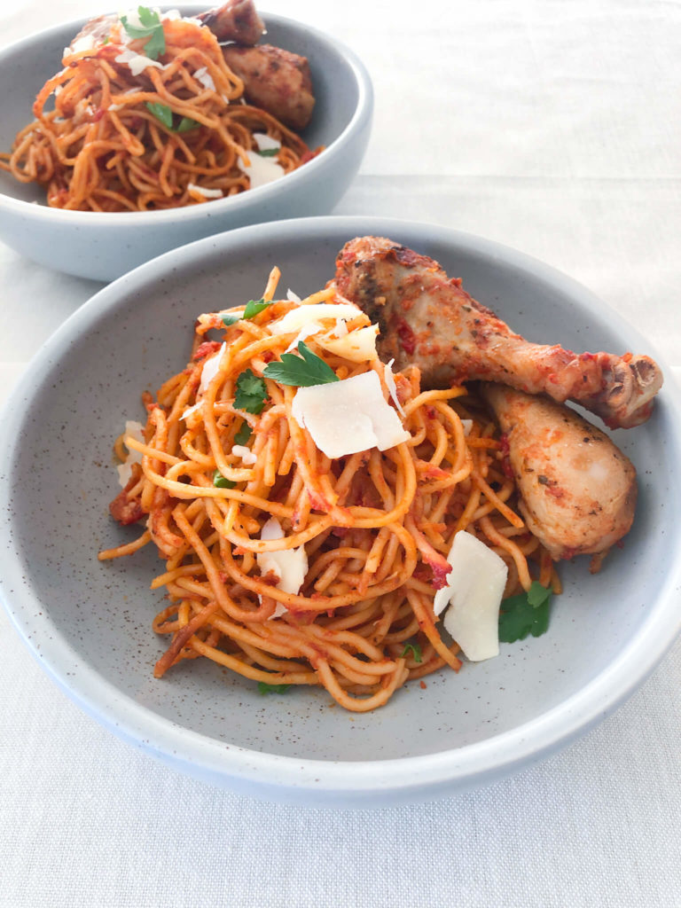 spaghetti with tomato sauce and chicken drumsticks in a light blue bowl.