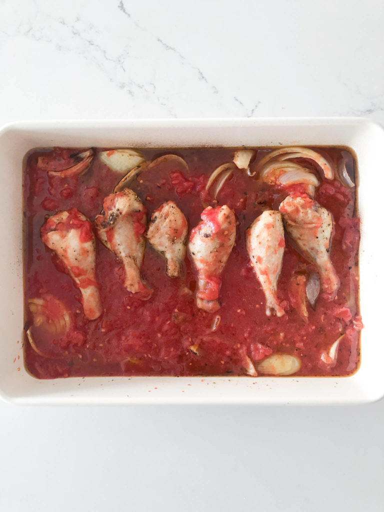 chicken drumsticks in tomato sauce with onions, garlic and seasonings in a baking dish