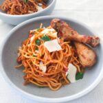 spaghetti with tomato sauce and chicken drumsticks in a blue bowl.