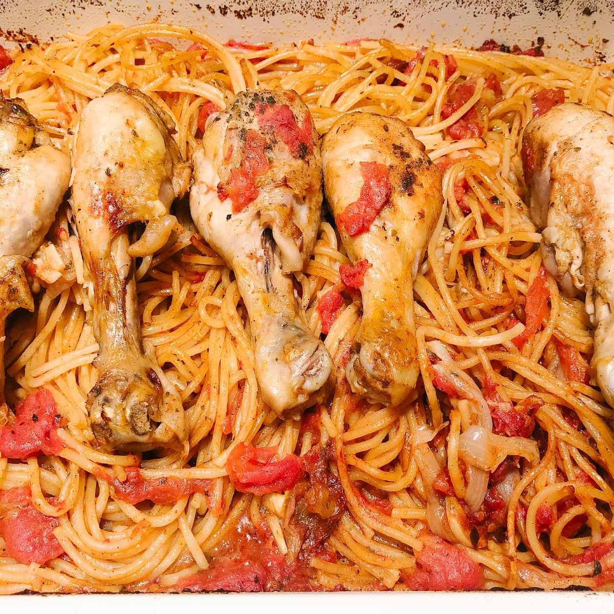 baked chicken drumsticks in a baking dish with spaghetti and tomato sauce.