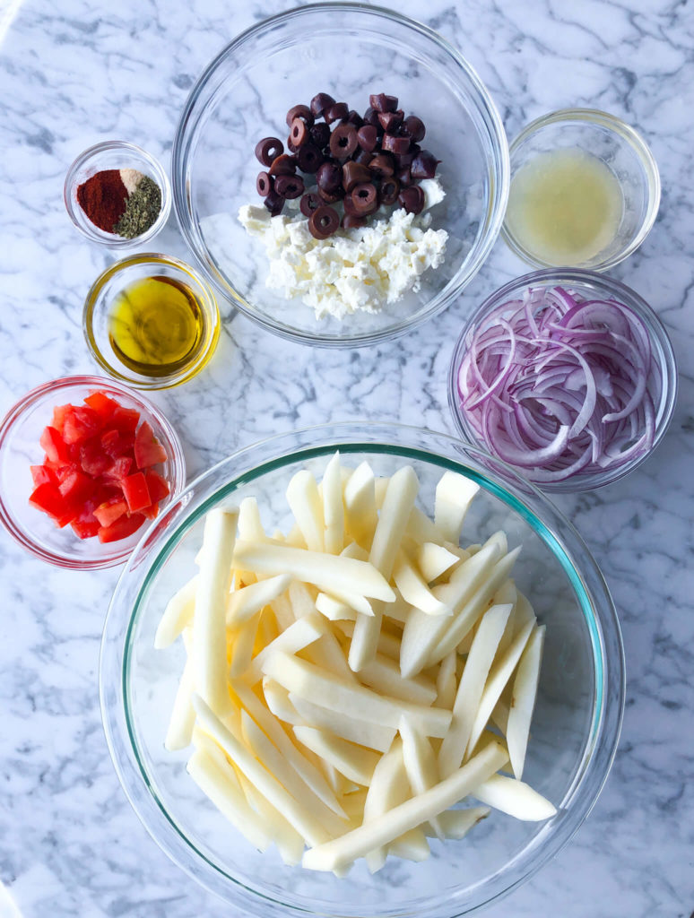 fries, diced tomatoes, seasonings, sliced red onion, crumbled feta, olive oil, and kalamata olives in clear bowls