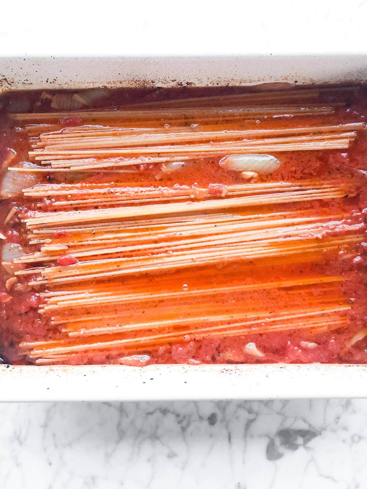 uncooked spaghetti and tomato sauce in a baking dish