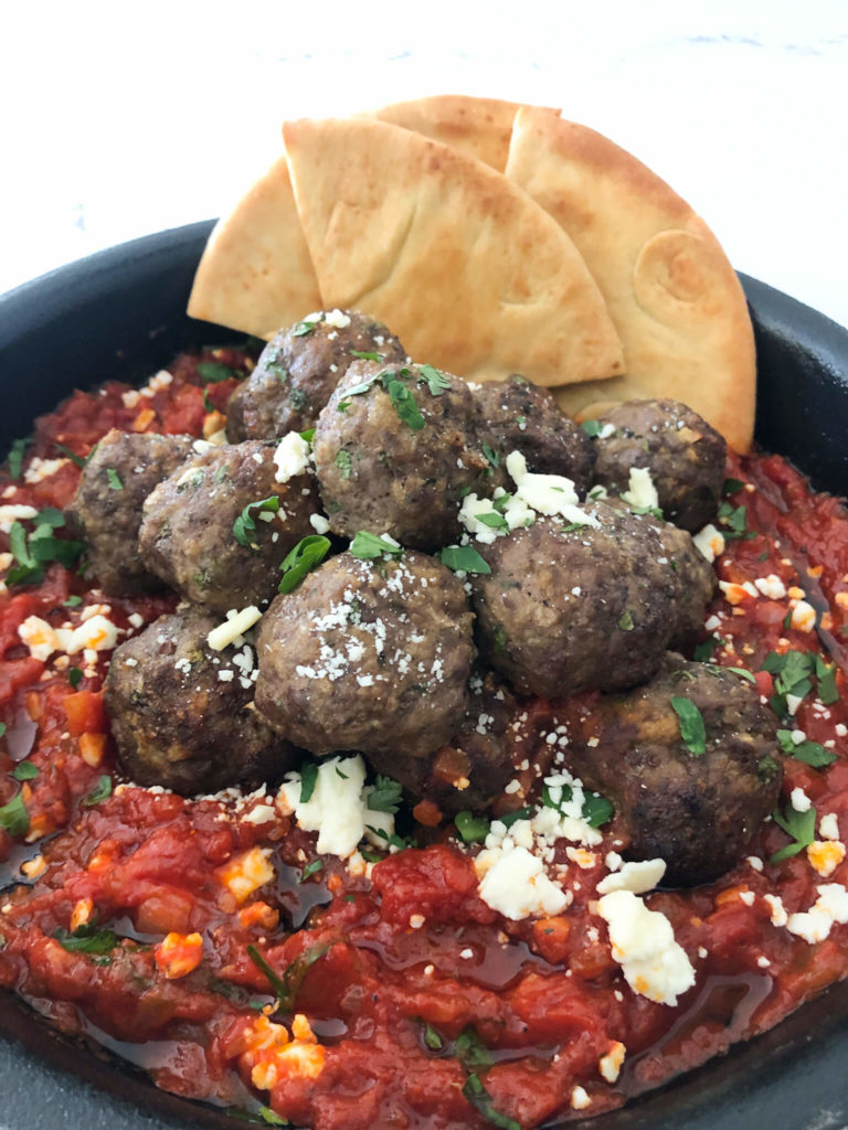 meatballs in marinara sauce topped with crumbled feta cheese and parsley