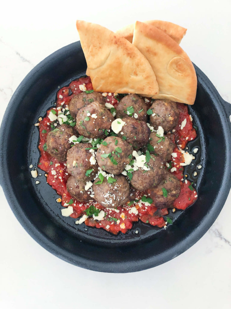 baked beef meatballs with marinara sauce topped with crumbled feta and parsley