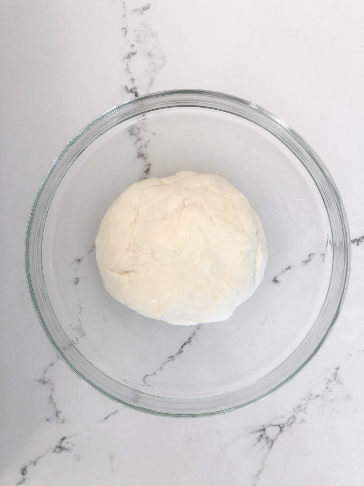 a round ball of pita bread dough in a large glass bowl.