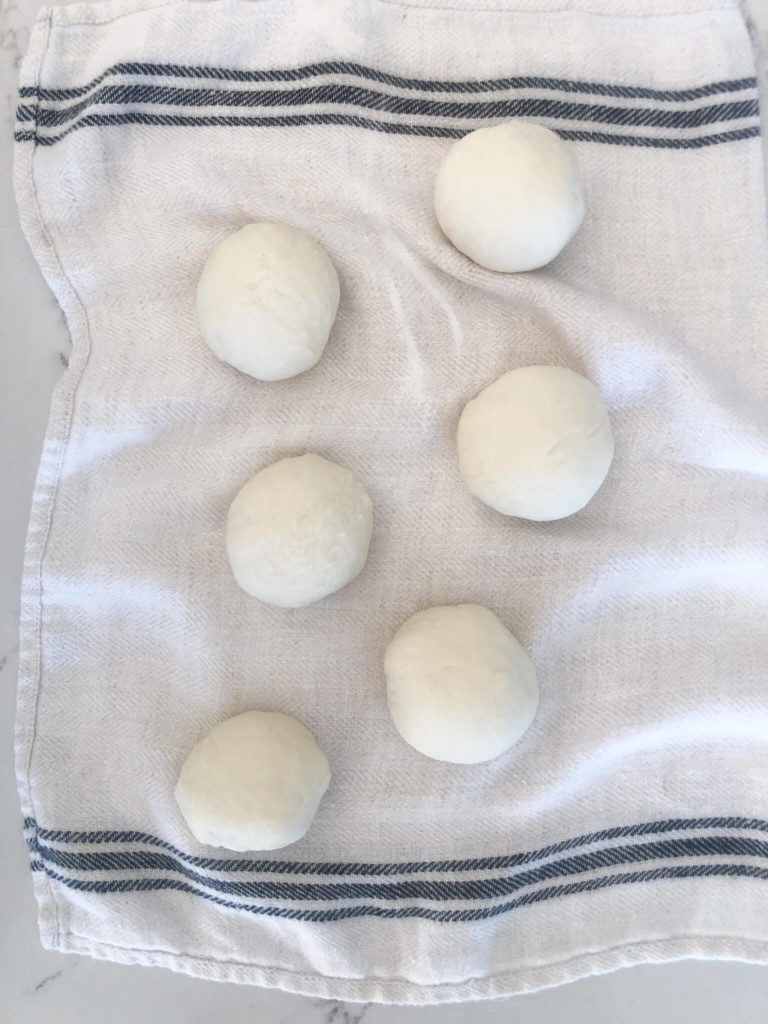 six pita bread dough balls on a clean white kitchen towel.