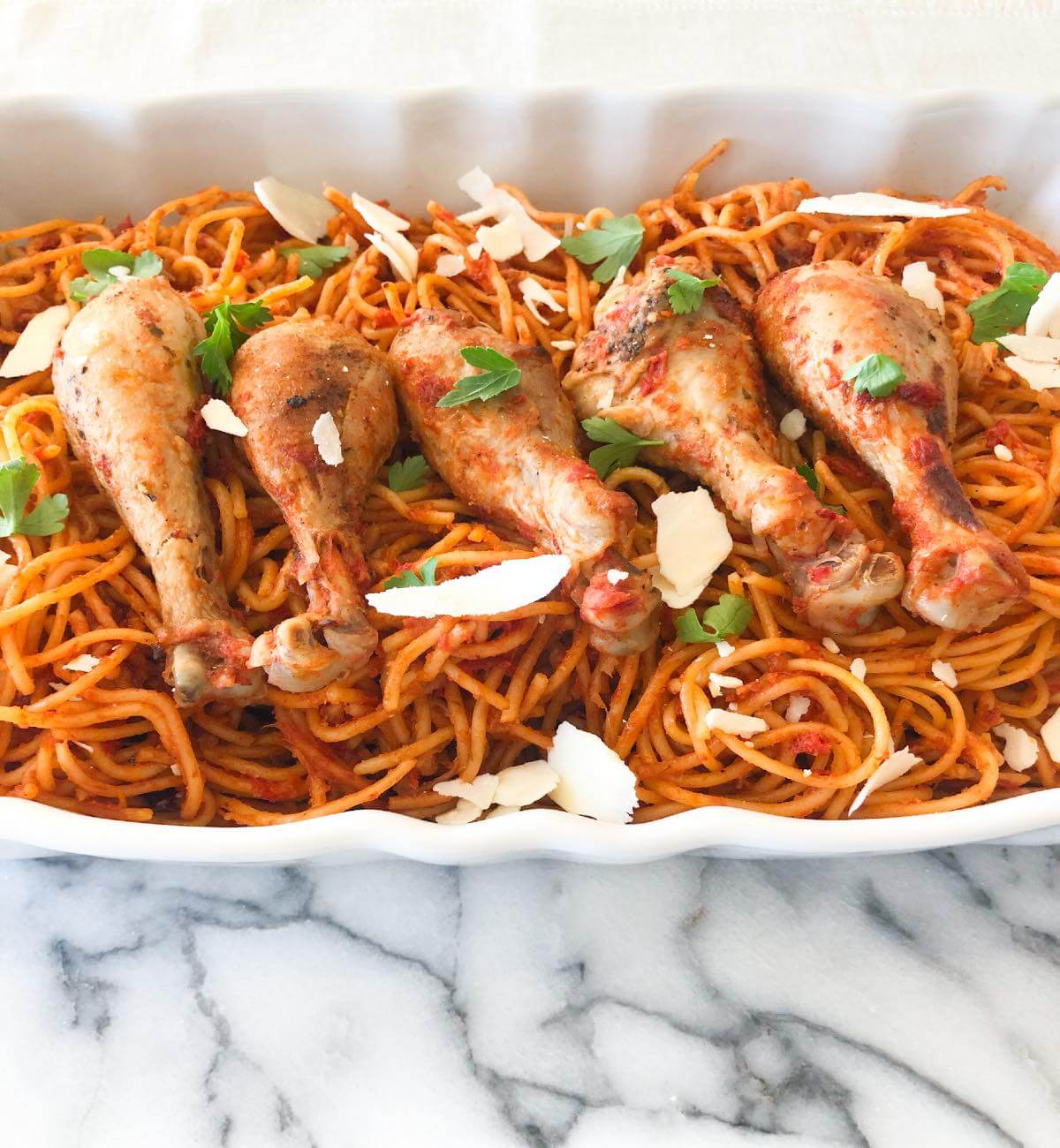 cooked chicken drumsticks and spaghetti with tomato sauce in a serving dish