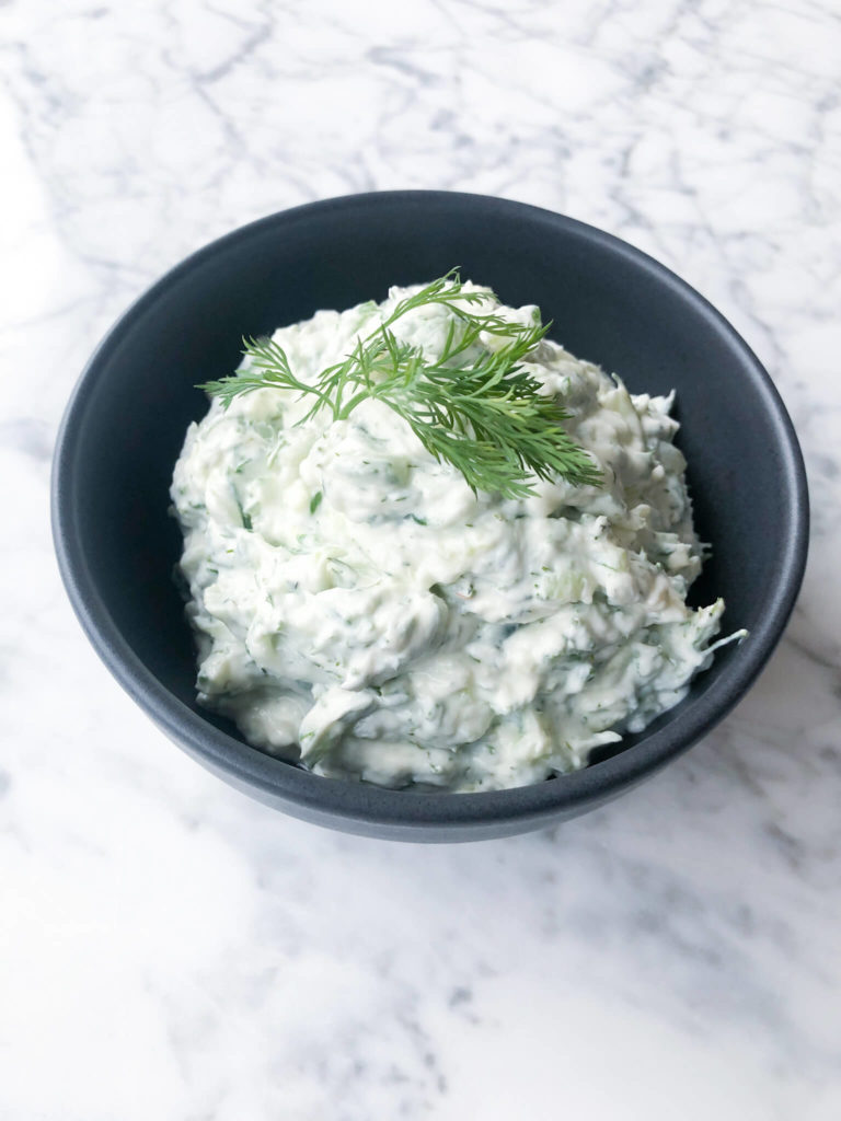 tzatziki sauce in a small black bowl topped with fresh dill.