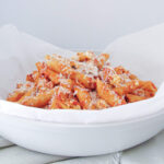 tomato penne pasta in a white bowl sprinkled with grated parmesan cheese.