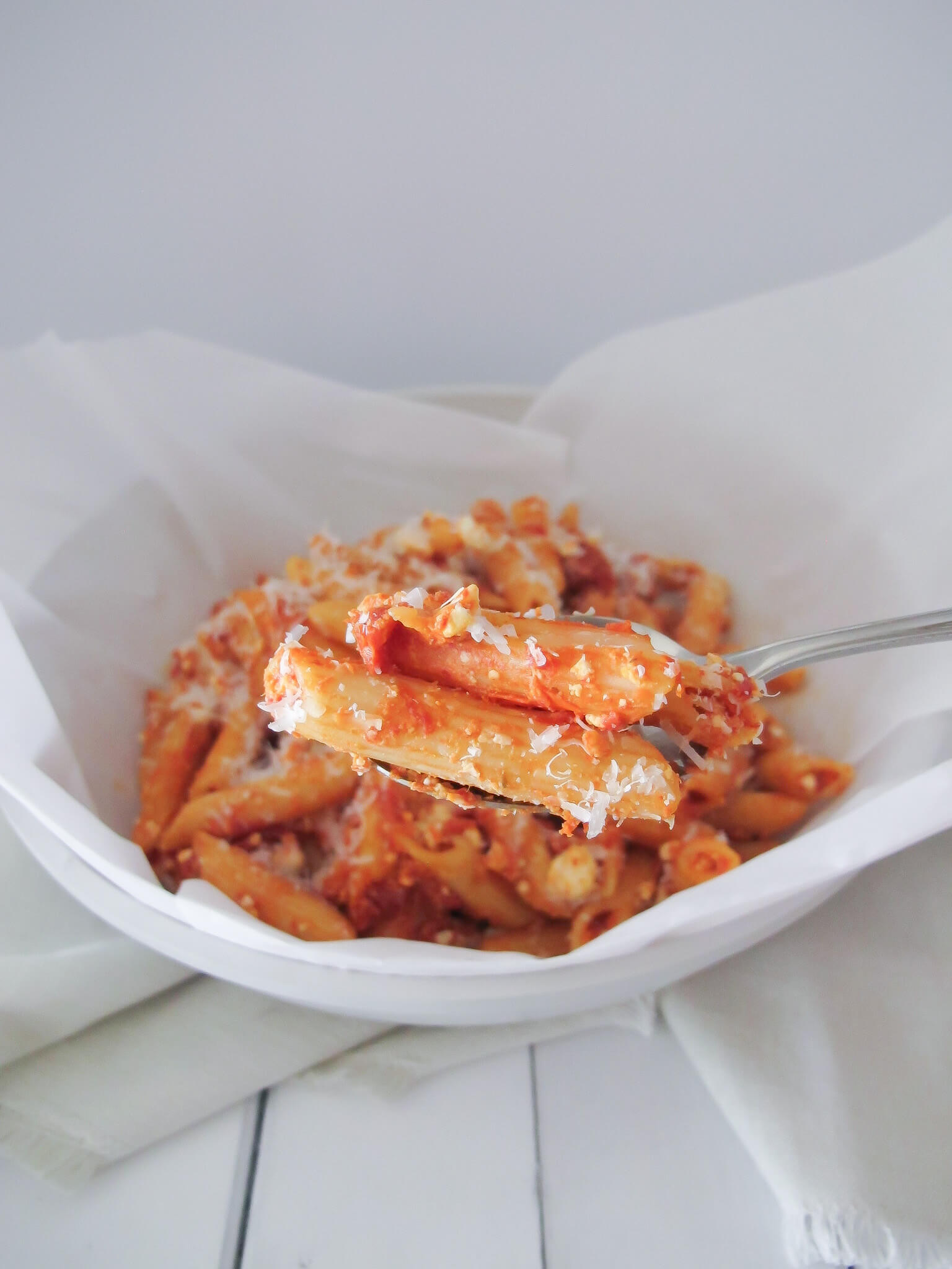A spoon of penne pasta with pink pasta sauce topped with crumbled feta and parmesan cheese