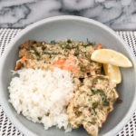 two pieces of salmon with mayo sauce served with white rice and a lemon wedge
