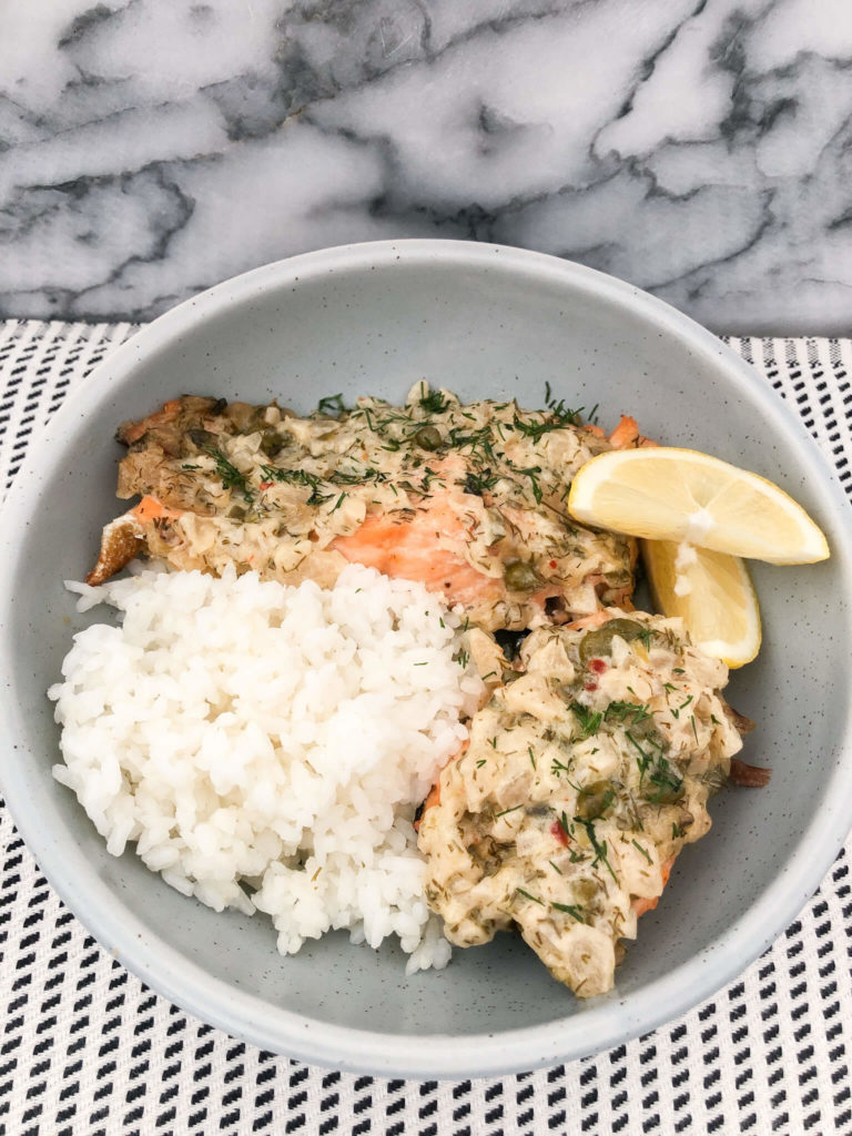 two pieces of salmon with mayo sauce served with white rice and a lemon wedge in a light blue bowl