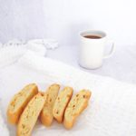 six pieces of lemon biscotti on a white kitchen towel with a cup of coffee.