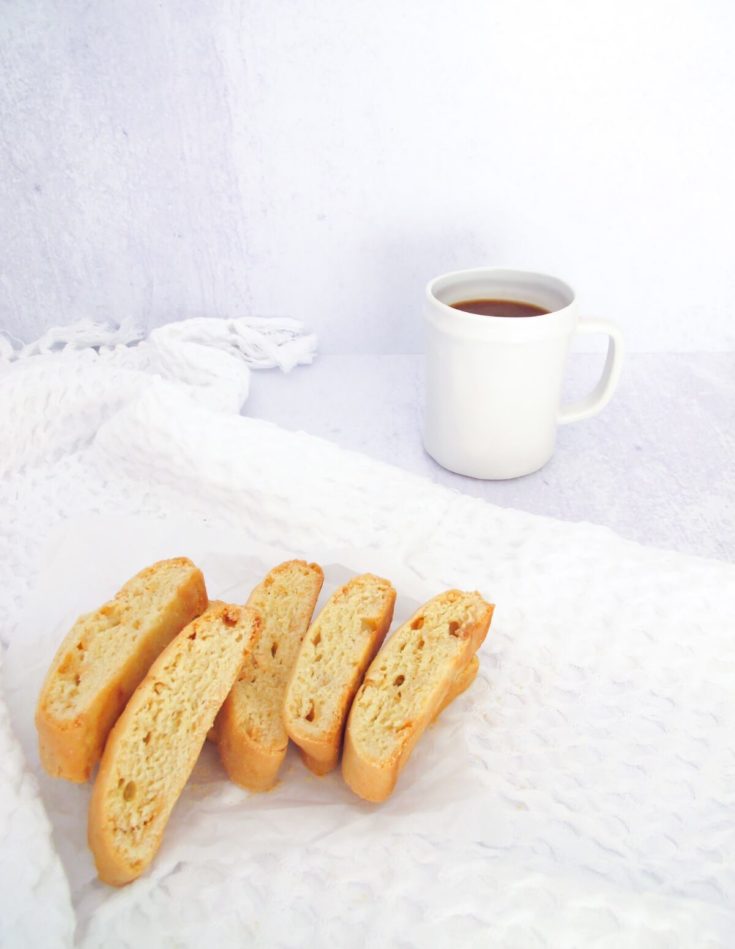 six pieces of lemon biscotti on a white kitchen towel with a cup of coffee.
