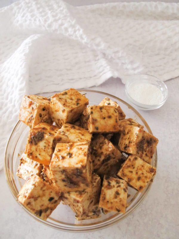 cubes of marinated Greek tofu in a glass bowl.