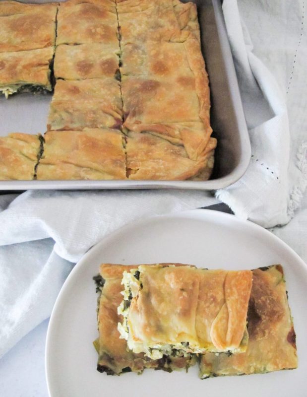 Greek spinach pie in a baking dish with three pieces of spinach pie on a white plate.