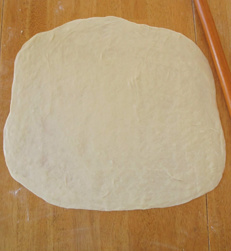 Spinach pie dough rolled out into a large circle with a rolling pin.