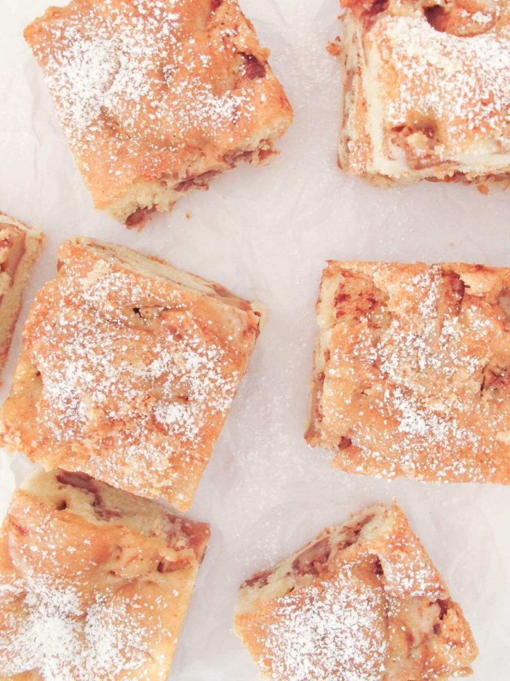 pieces of apple spice cake on parchment paper sprinkled with icing sugar.