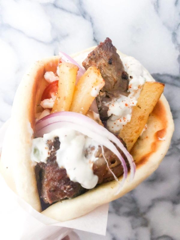 pork souvlaki wrapped in pita bread, with tzatziki, fries, sliced tomatoes, and red onions.