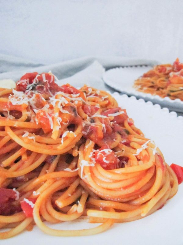 spaghetti with spicy tomato sauce on a white plate with parmesan cheese.