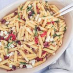 penne pasta with sundried tomatoes, feta cheese, kalamata olives in a white baking dish.