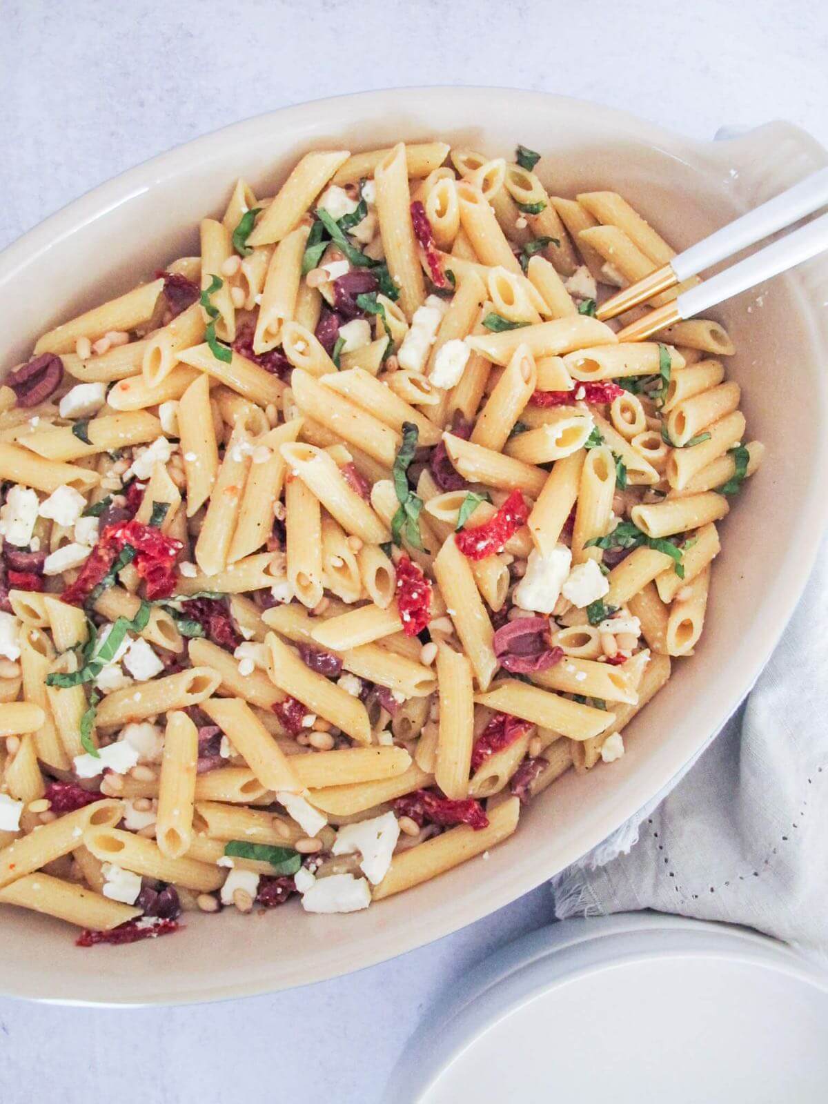 penne pasta with sundried tomatoes, feta cheese, kalamata olives in a white baking dish.