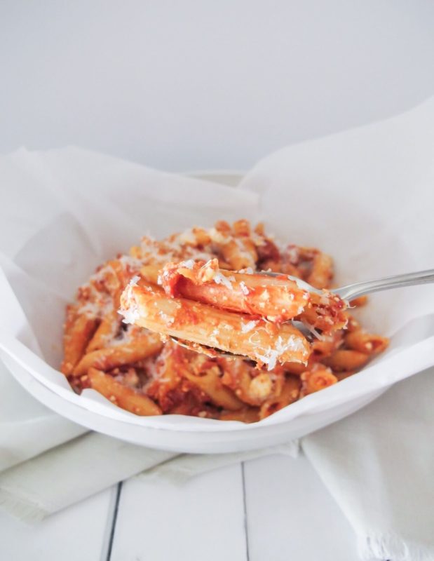 A bowl of penne pasta with pink pasta sauce topped with crumbled feta and parmesan cheese.