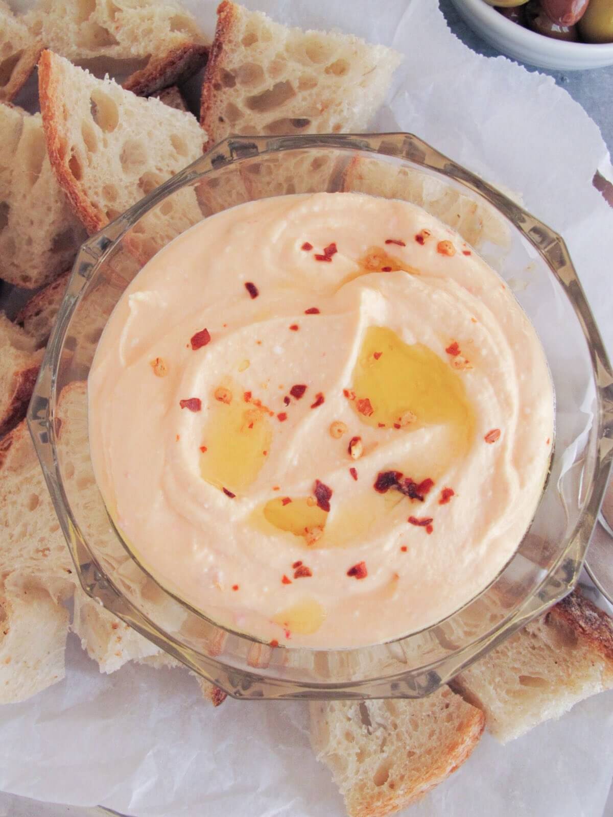 spicy feta cheese dip in a glass container surrounded by pieces of bread.
