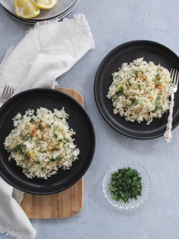 two plates of greek rice on black plates and topped with fresh dill and parsley.