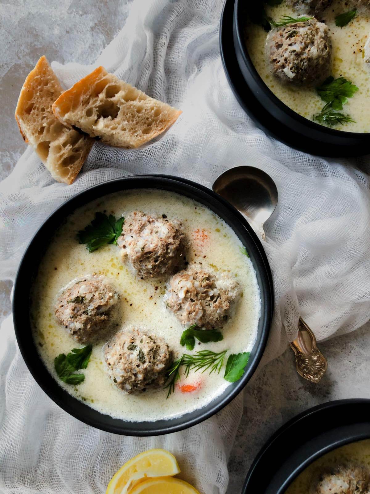 Greek meatball soup in a black bowl with fresh parsley. 