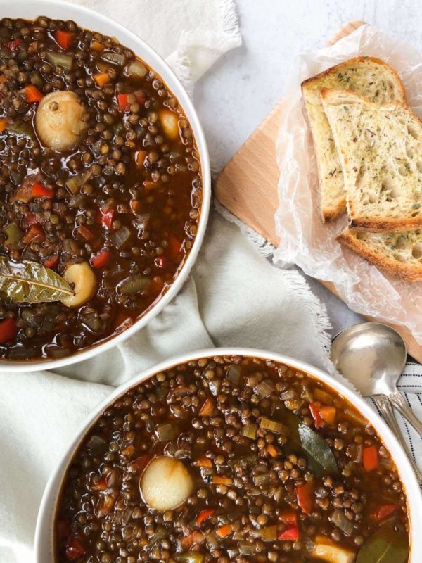 Greek lentil soup in two white bowls with toasted bread.