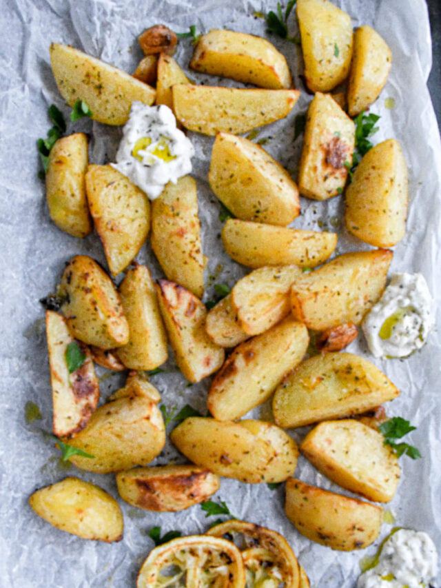 Greek potatoes on a baking dish with tzatziki and Italian parsley.