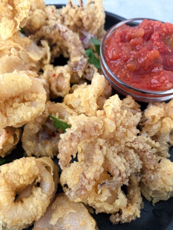 Deep fried calamari served with salsa dipping sauce on a black plate.
