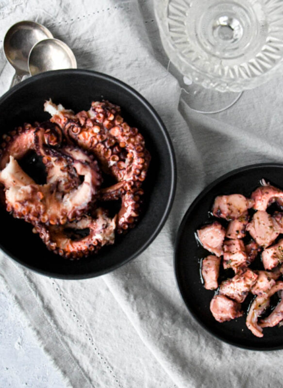 Small pieces of Greek marinated octopus on black plates.