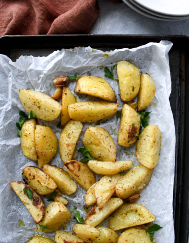 Greek potatoes on white parchment paper on top of a black baking dish.
