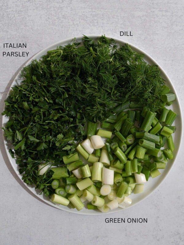 Fresh dill, Italian parsley, and green onions diced on a white plate.