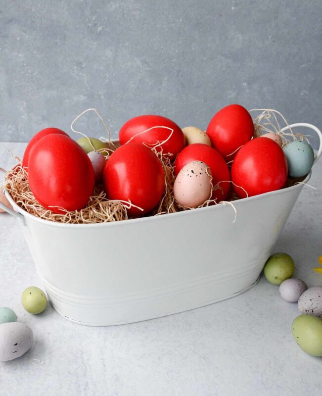 Red Greek Easter eggs in a white basket with mini pastel coloured eggs.