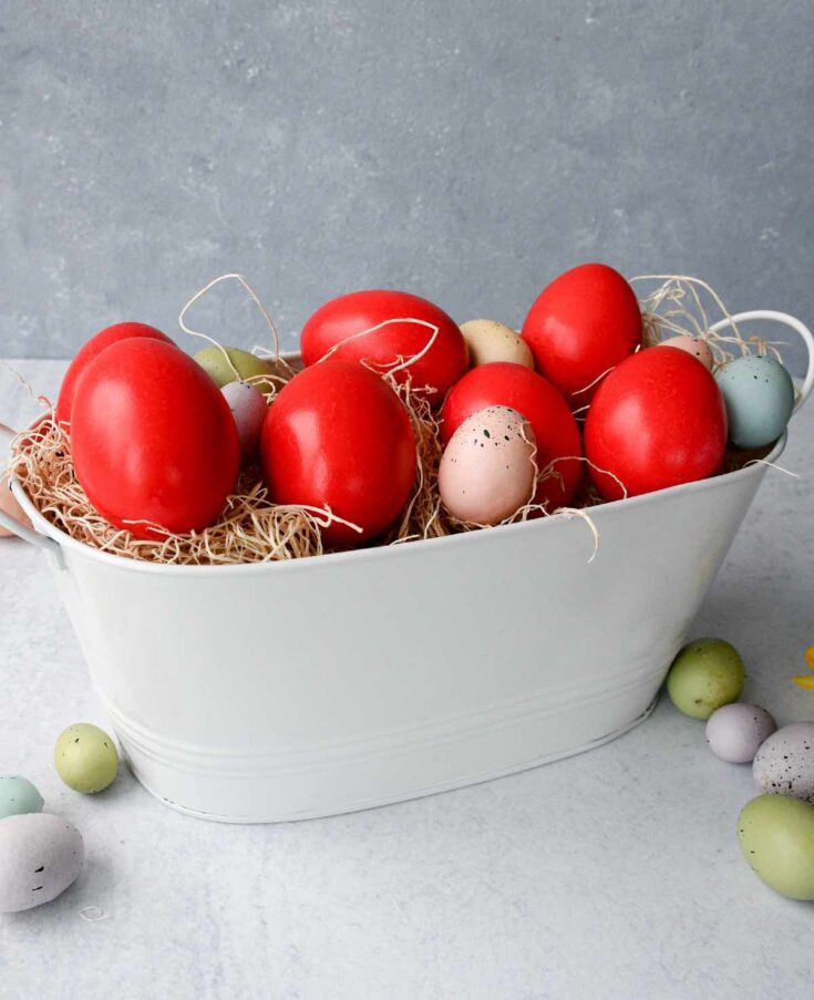 Red Greek Easter eggs in a white basket with mini pastel coloured eggs.