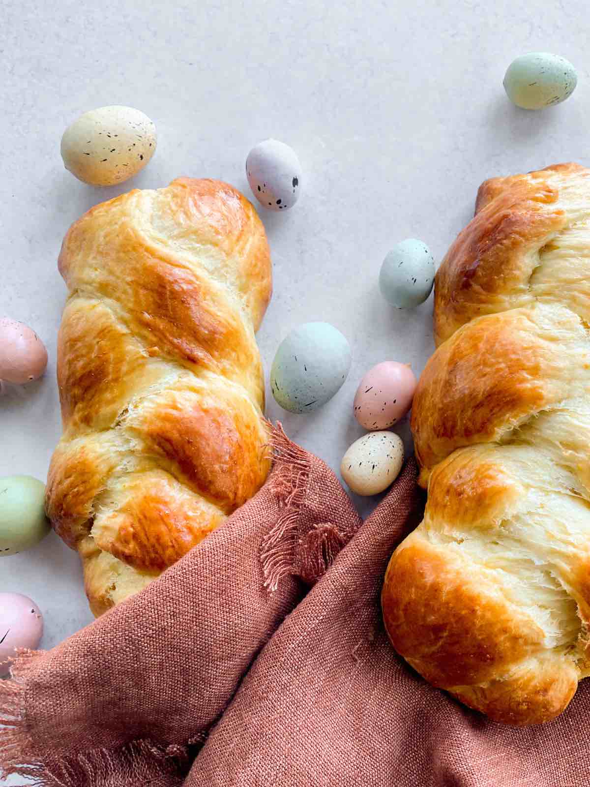Two pieces of tsoureki (Greek Easter bread) on a white counter with pastel coloured easter eggs.