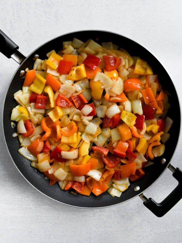 sautéed yellow bell peppers, red peppers, orange peppers, and onions in a black frying pan.