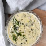 creamy dill sauce in a clear small glass bowl with fresh dill and lemon zest on top.