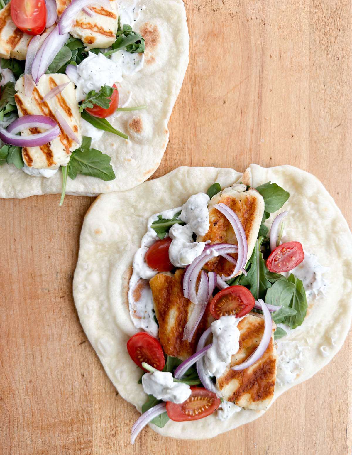 open faced halloumi cheese souvlaki with garlic pita bread, tzatziki, tomatoes, and sliced red onions.