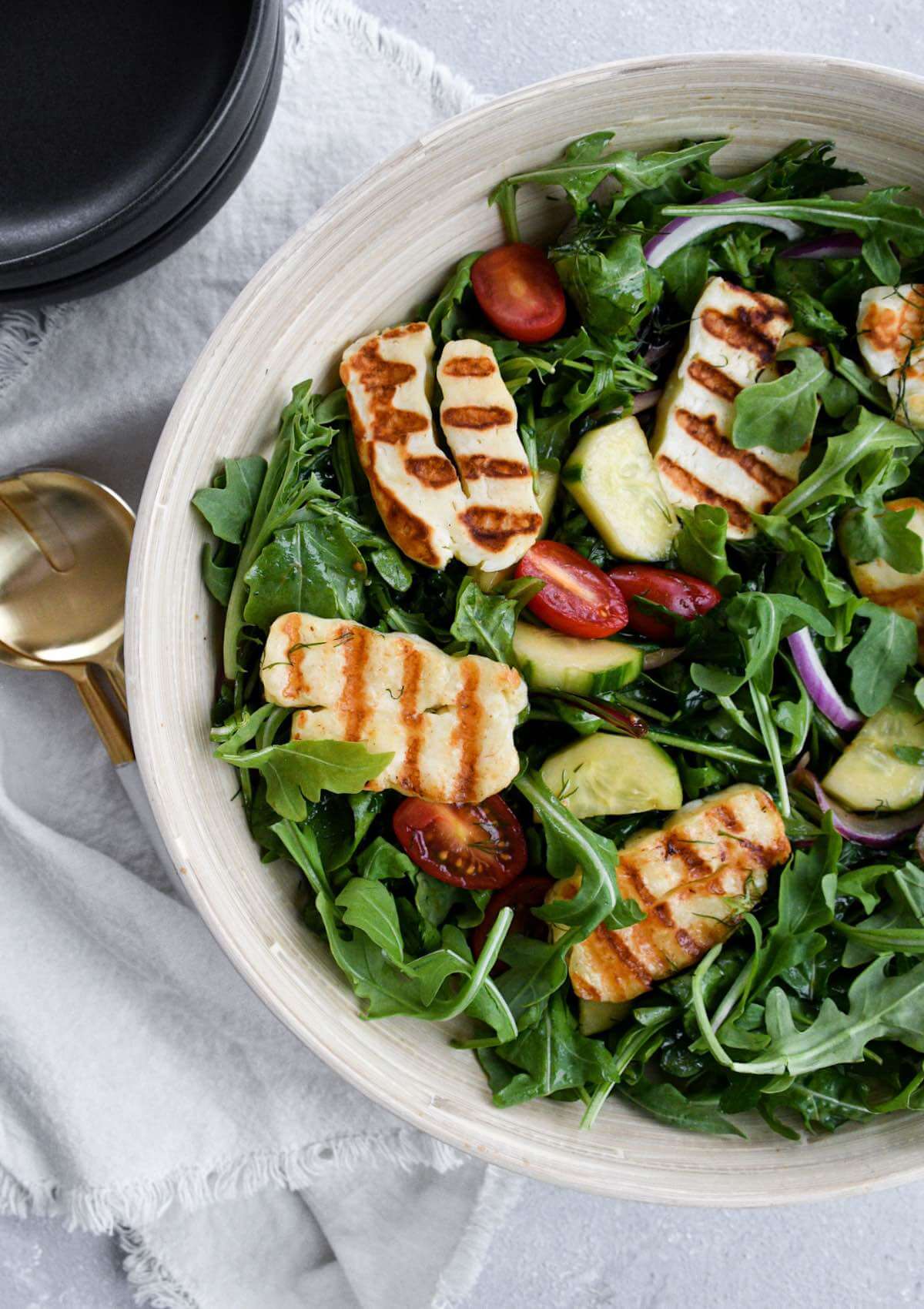 halloumi cheese salad with grilled halloumi, fresh greens, tomatoes, onions, and dill in a wooden bowl.