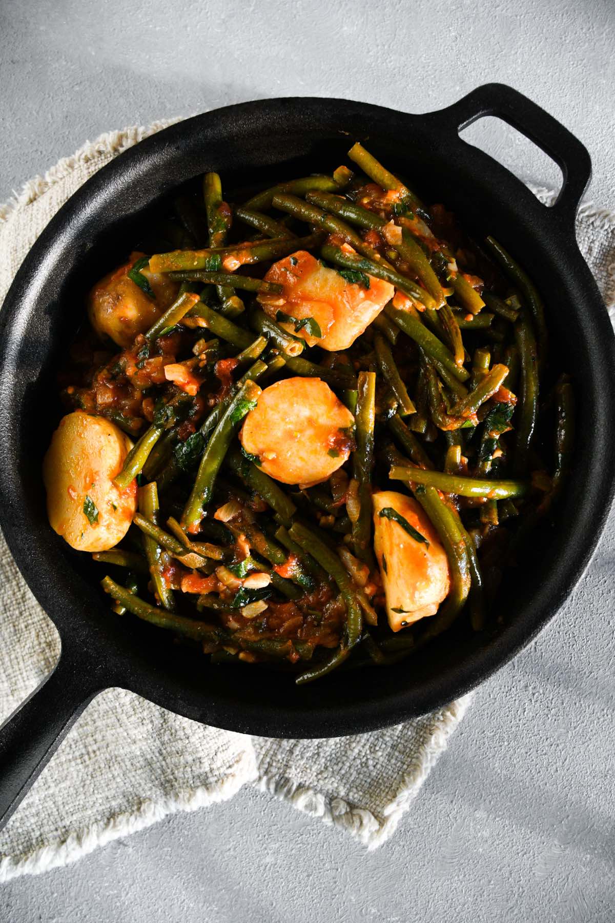 fasolakia (Greek green beans) with potatoes and tomato sauce displayed in a black cast iron skillet.